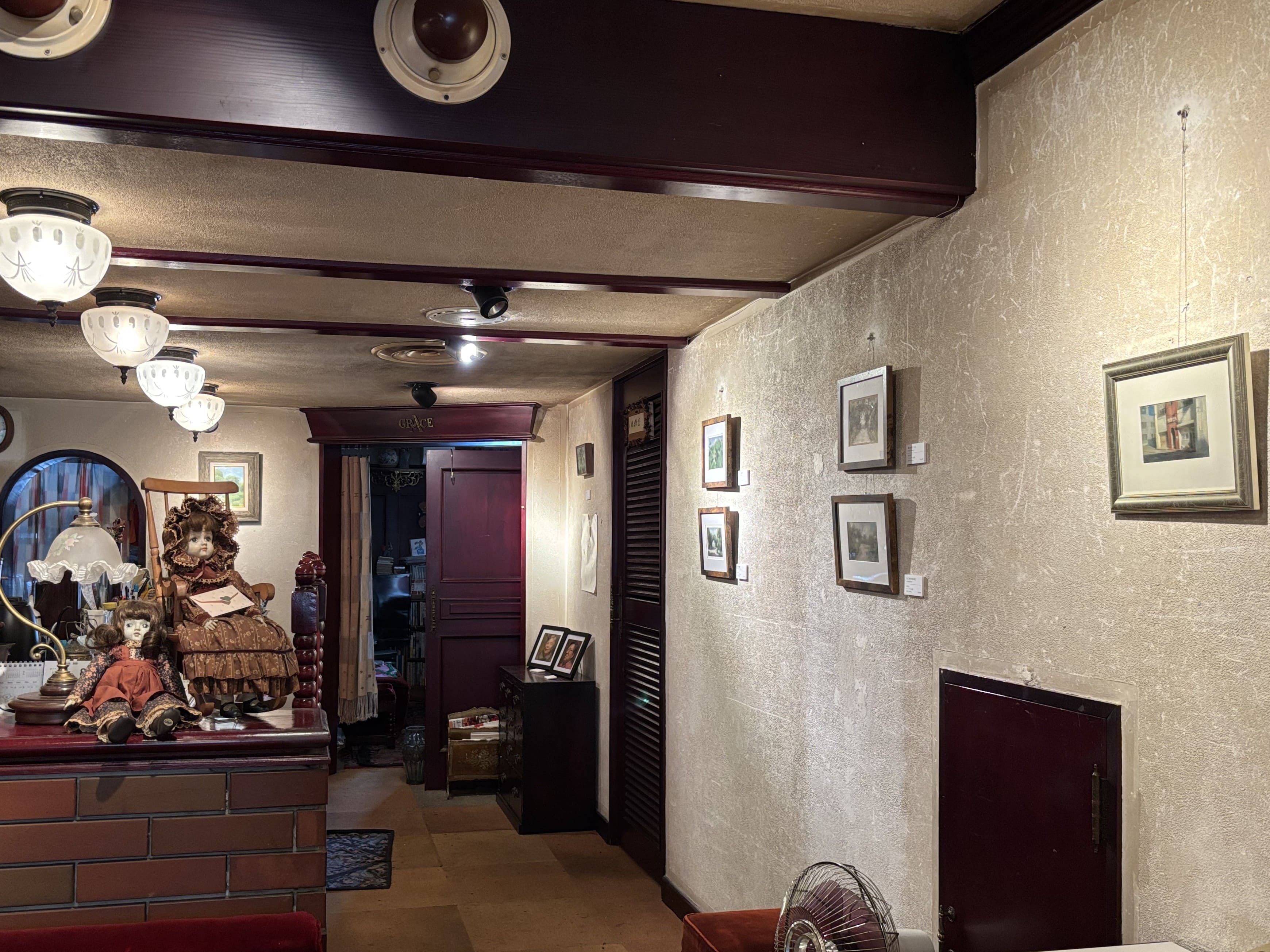 店内の白い壁に小さめの風景画が複数展示されている。カウンターには椅子に座った人形が飾られている。